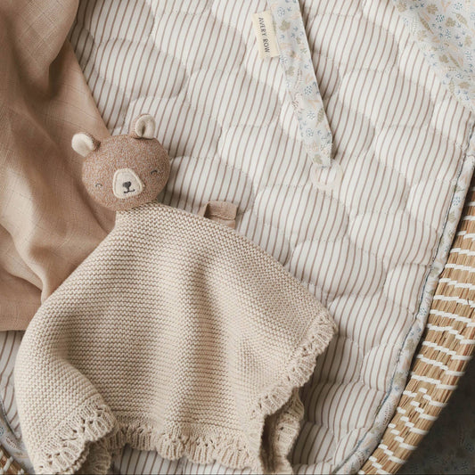 Knitted blanket with a teddy bear toy on a striped surface
