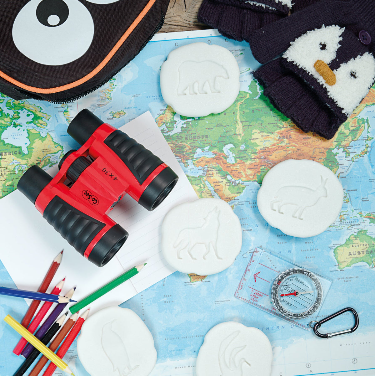 Children's penguin and polar themed items including binoculars, compass, polar animal sensory stones and crayons on a map.