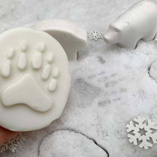 White animal-shaped stones, including a bear and a paw print, displayed on a snowy textured surface with decorative snowflakes.