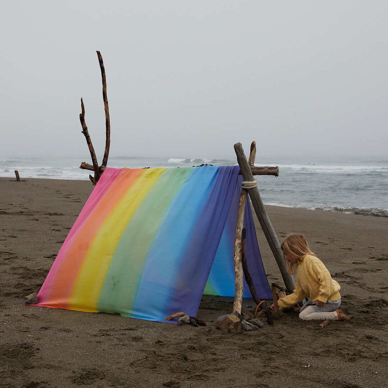 Child playing with a rainbow silk tent on a beach