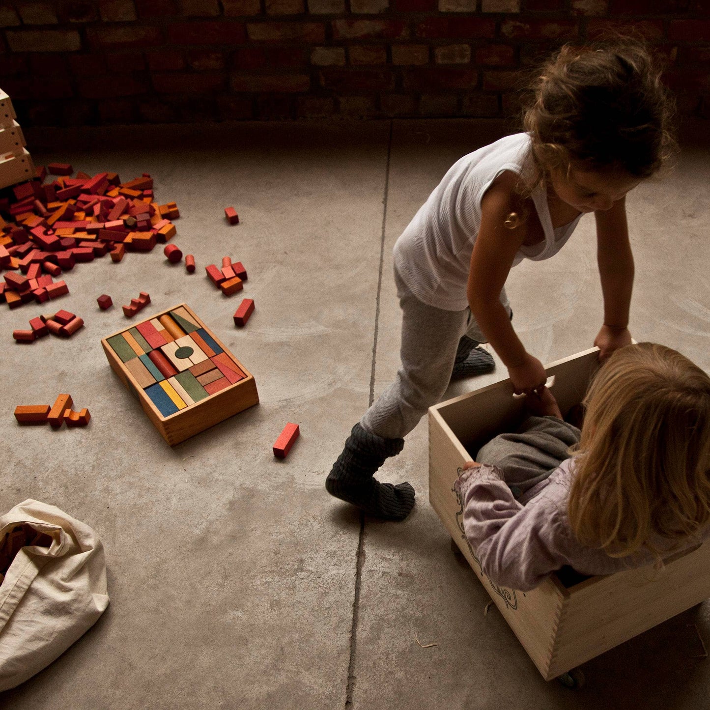 Two children playing with wooden blocks in a room with a brick wall.