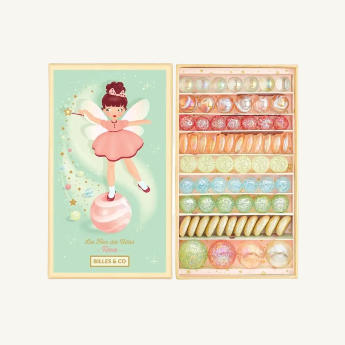 A boxed set of decorative marbles displayed open next to its illustrated lid. The lid shows a fairy in a pink dress standing on a pink marble against a pale mint background, with the text 'Die Frau des Billes Rose' and 'BILLES & CO' at the bottom.