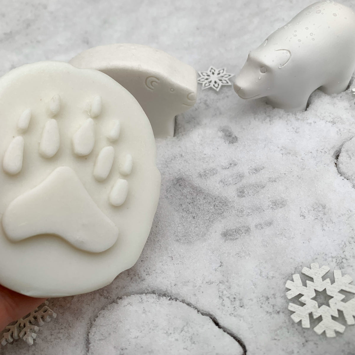 White animal-shaped stones, including a bear and a paw print, displayed on a snowy textured surface with decorative snowflakes.