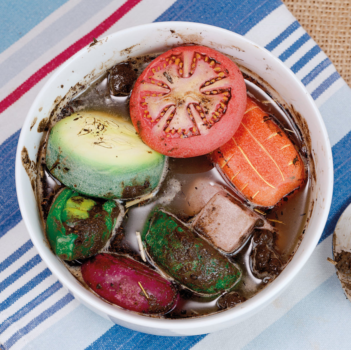 Bowl of soup with colorful play stone vegetables on a striped tablecloth