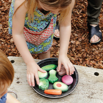 Children playing with toy play stone vegetables on a wooden surface outdoors.