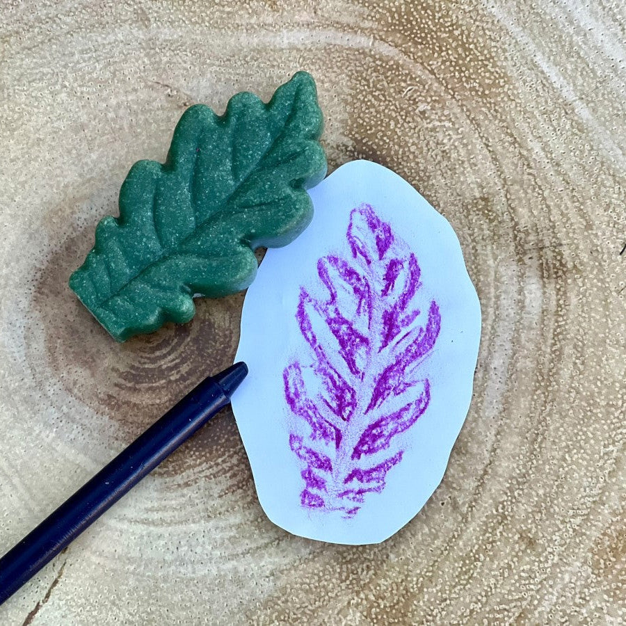 A small white leaf sensory stone or snext to a purple leaf imprint, placed on a natural wood slice background