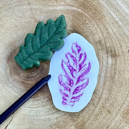 A small white leaf sensory stone or snext to a purple leaf imprint, placed on a natural wood slice background