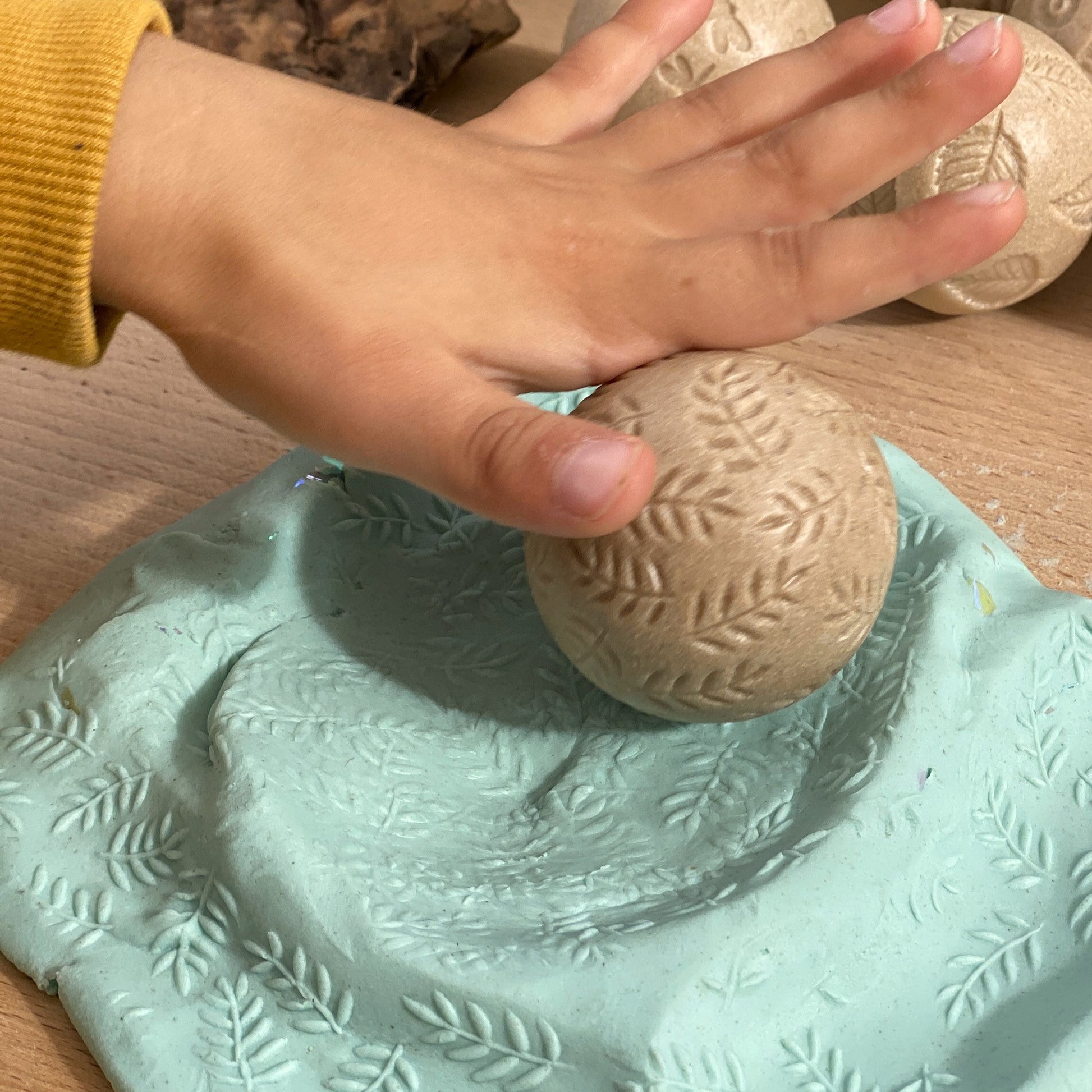 Hand interacting with a textured green surface and stone-like object on a wooden background