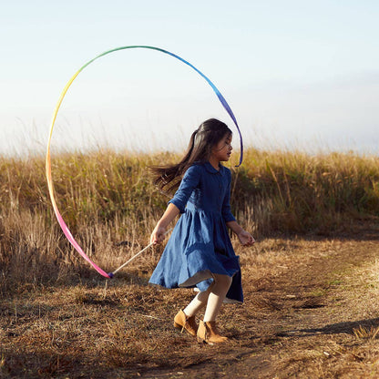 Girl in a blue dress playing with a colorful streamer in a field