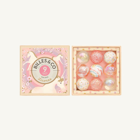 Billes & Co Mini Unicorn Box containing 9 glittery shooter marbles, shown with its illustrated pink and gold lid next to the box containing the clear, pink, and multicolored glitter spheres.