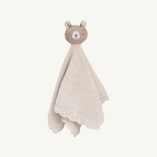 A knitted baby soothing blanket featuring a plush teddy bear head with a textured beige face and ears, attached to a cream-colored fringed knitted body.