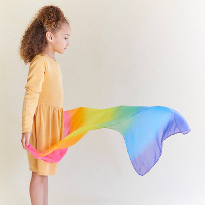 Child wearing a yellow dress with a rainbow silk against a plain background