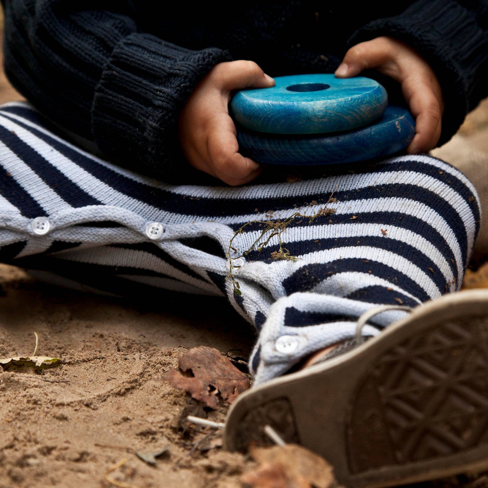 Person wearing striped pants and brown shoes holding a blue object in a natural setting.