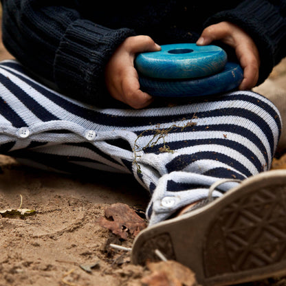 Person wearing striped pants and brown shoes holding a blue object in a natural setting.