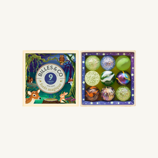 A boxed set of nine decorative glass Forest Magic shooter marbles displayed beside its illustrated lid. The lid features woodland artwork with the brand name Billes & Co and the text '9 carats pour la forêt magique.