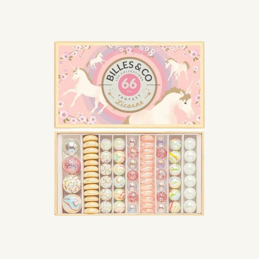 An open gift box of Billes & Co. 66 unicornd marbles, showing a variety of colorful, decorated pieces arranged in a box set against a plain cream background.