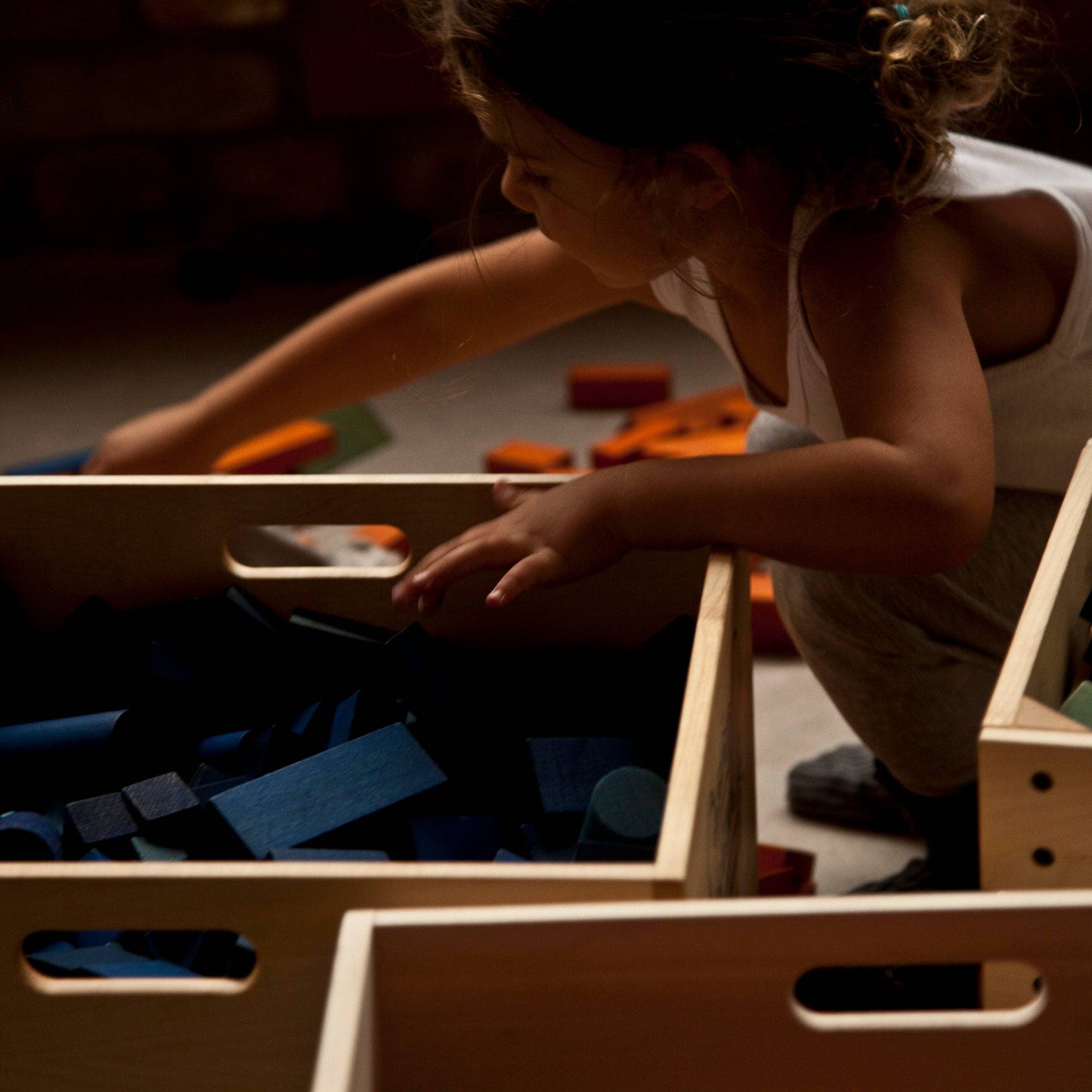 Child playing with toys in wooden crates on a floor.