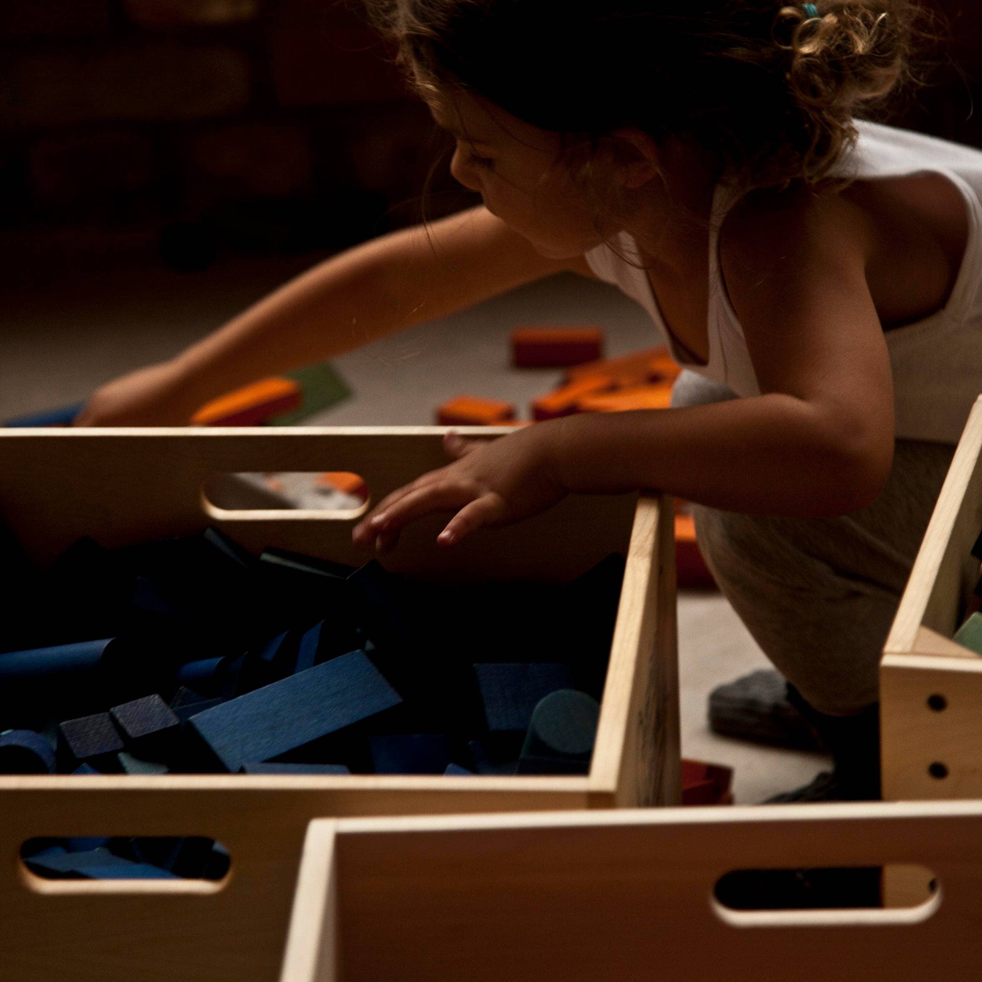 Child playing with toys in wooden crates on a floor.