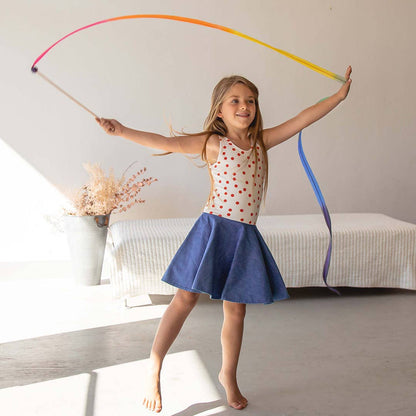 Young girl playing with a colorful streamer indoors.