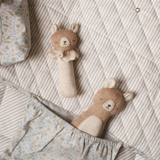 Two plush baby organic rattle toys shaped like bears, nestled in a striped and floral baby blanket.