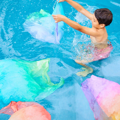 Child playing with colorful silk scarves in a pool
