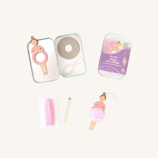 A flat-lay product photo of a 'Cotton Twist Prima Ballerina' DIY home decoration kit. The kit includes a small metal tin with a ballerina-shaped ring cutter, a spool of white thread, a wooden needle, and another tin showing the purple 'Prima Ballerina' packaging, all arranged on a cream background 
