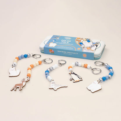 A children's bead and charm craft kit displayed with four completed polar animal keychains and the blue storage box behind them on a light beige background. The kit includes beaded strands with metal keyrings and small animal charms, and the packaging shows polar bear illustrations.