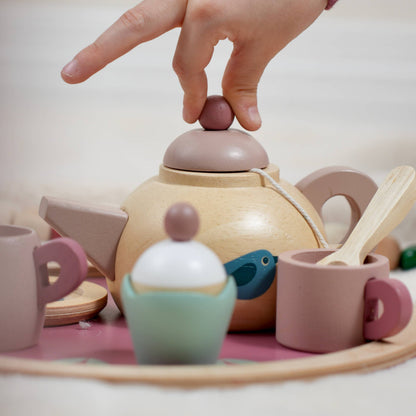 Child's hand interacting with a toy tea set on a light surface.