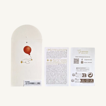 Three flat product components on a white background: a cream-colored arched pouch with a red balloon and white goose illustration, a small instruction card, and a white product card with branding and QR code for Senger Naturwelt.