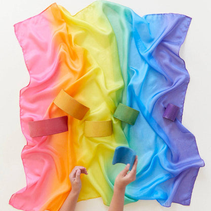 Colorful rainbow cape with children's hands holding it on a white background