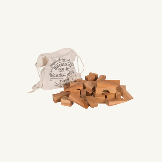 Wooden building blocks in various shapes scattered in front of a cream-colored fabric drawstring bag printed with 'Original No. 9 Wooden Doll Toys'.