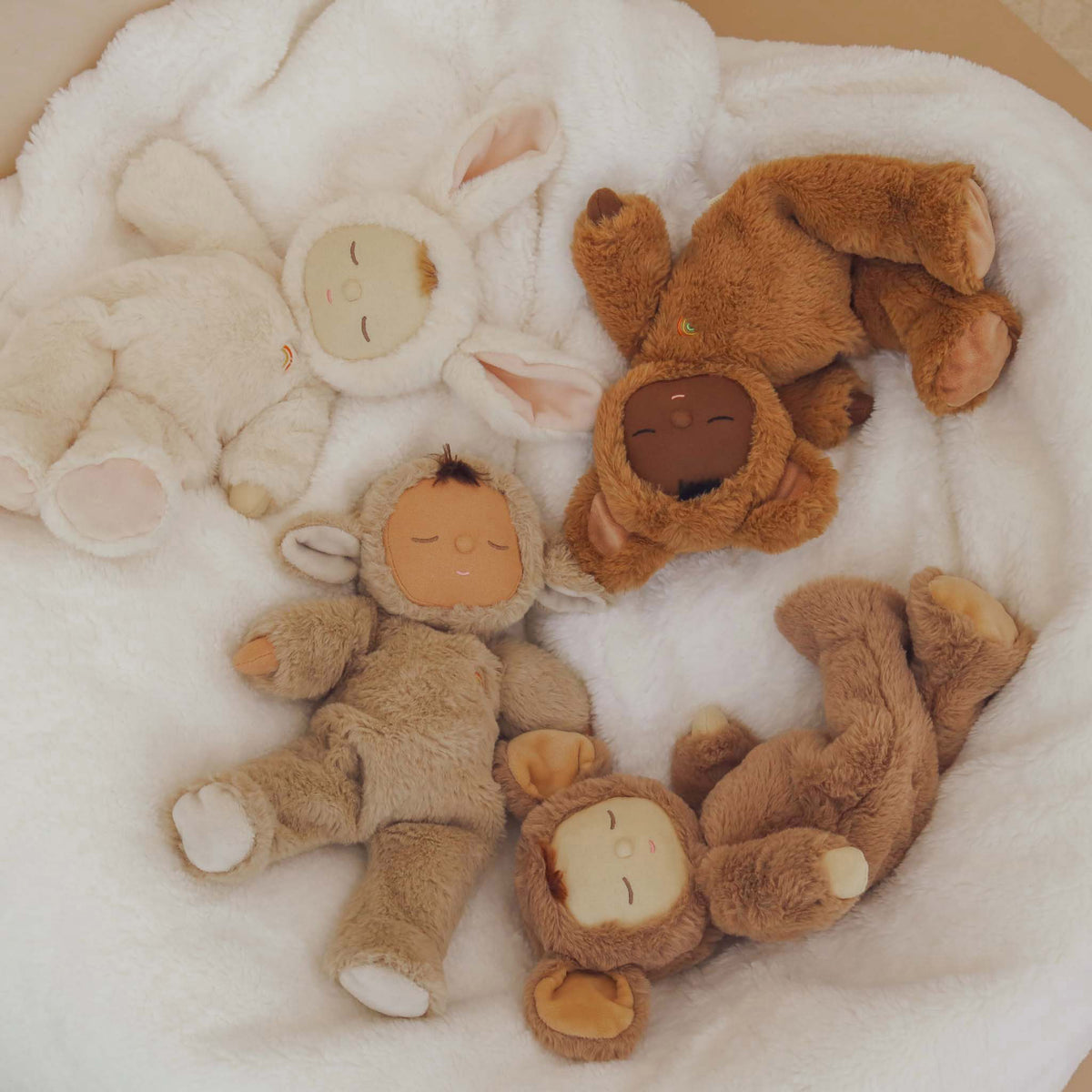 Four soft toys with sleeping faces on a white blanket