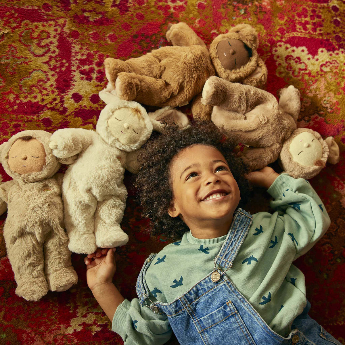 Child surrounded by stuffed animals on a patterned rug