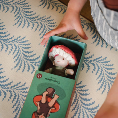 Person opening a box with a mushroom-shaped toy inside on a patterned surface