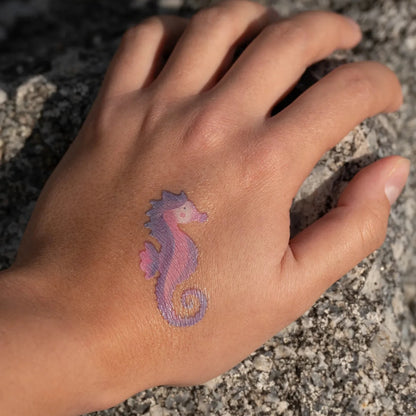 Hand with a pink seahorse tattoo on a rocky surface
