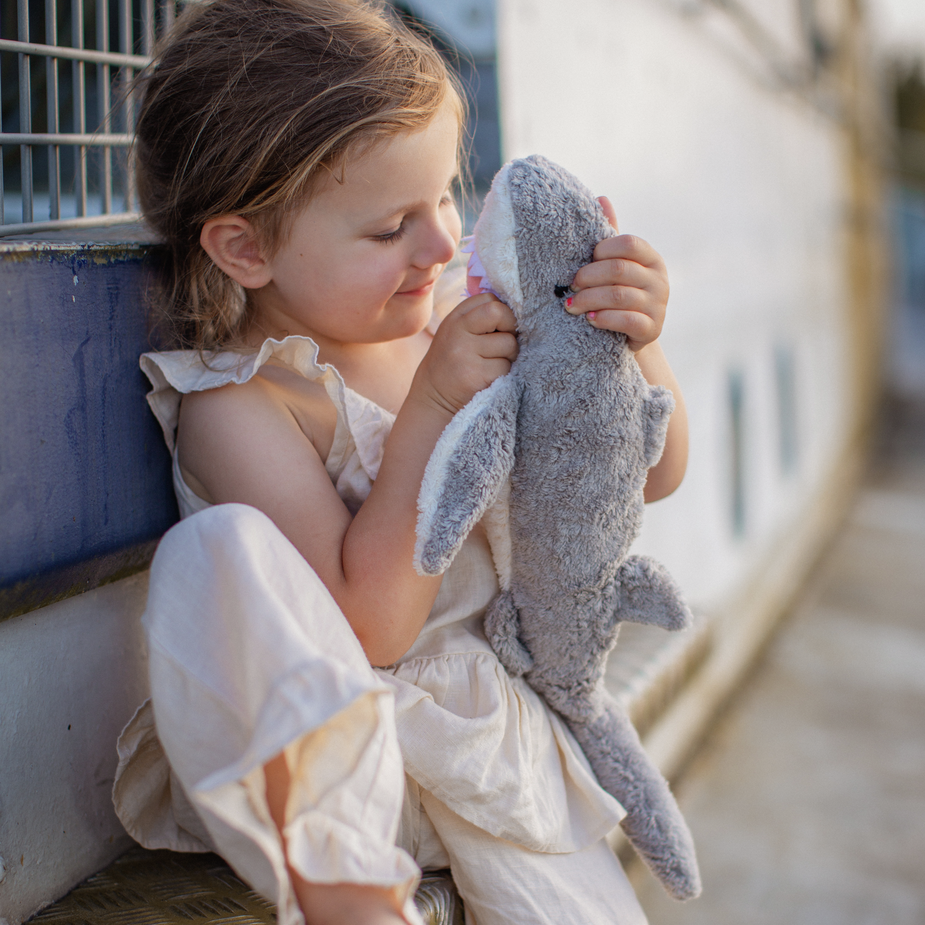 Child holding a shark plush toy against a wall.