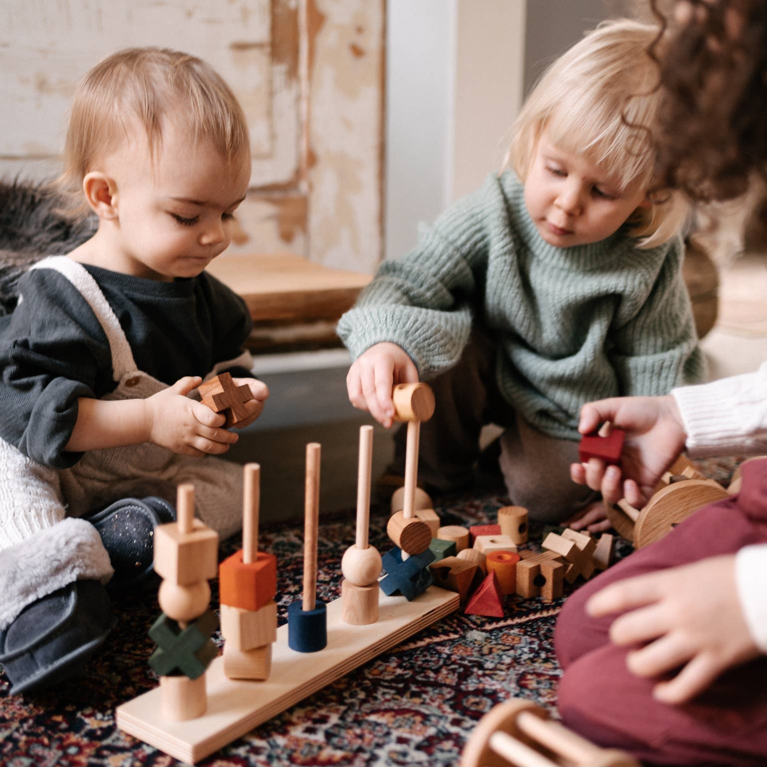 Two children playing with wooden toys on a patterned rug.