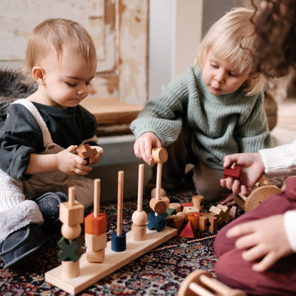 Two children playing with wooden toys on a patterned rug.