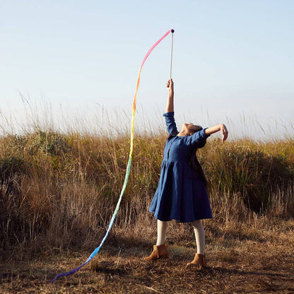 Child in a blue dress holding a rainbow streamer in an open field