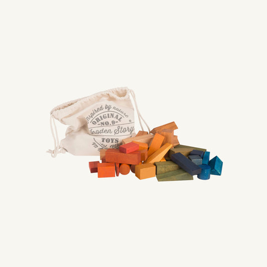 A set of colorful wooden building blocks spilled out from a cream-colored canvas drawstring bag. The bag features printed text reading 'Inspired by nature Original No.