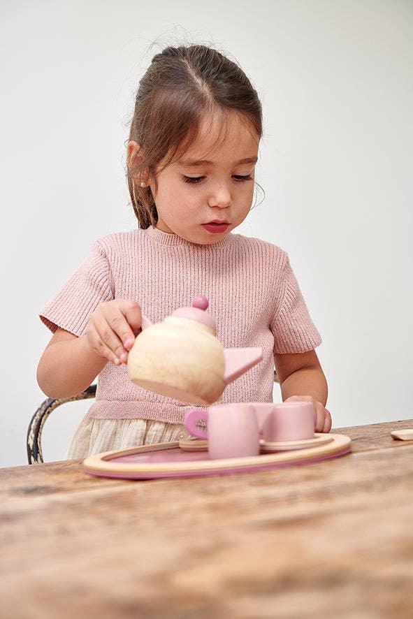 Young girl playing with a wooden tea set on a wooden table.