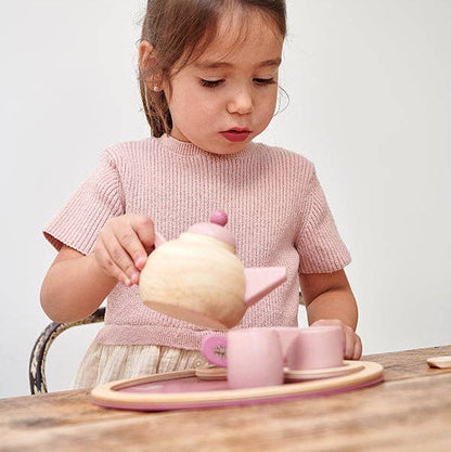 Young girl playing with a wooden tea set on a wooden table.