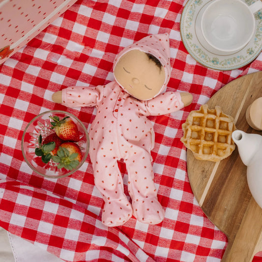 Dozy Dinkum doll in pink outfit on a red and white checkered tablecloth with waffles and strawberries.