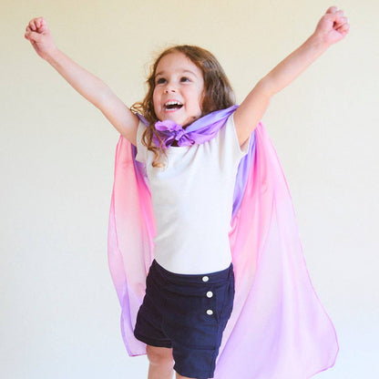 Child wearing a colorful cape with arms raised against a plain background