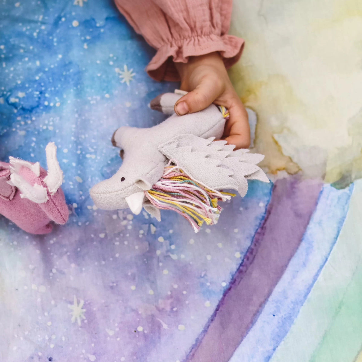 Child's hand holding a soft toy on a colorful  rainbow play cloth fabric background