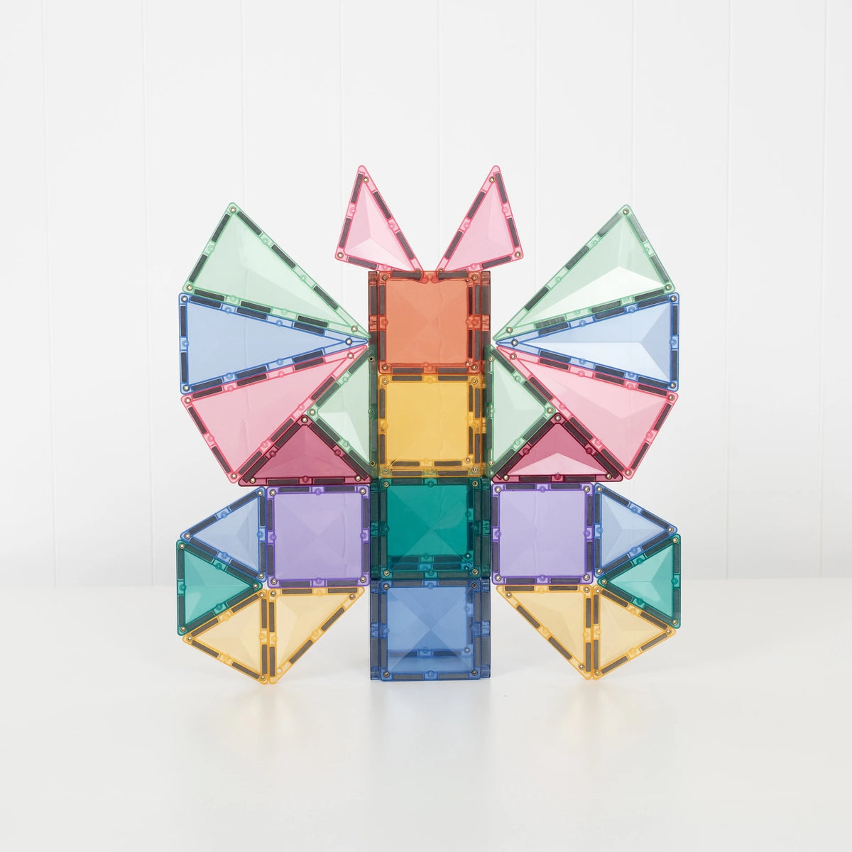A colorful magnetic tile structure built into a butterfly-like shape, made from translucent square and triangular pieces in pink, blue, green, yellow, and purple, photographed on a clean white background.