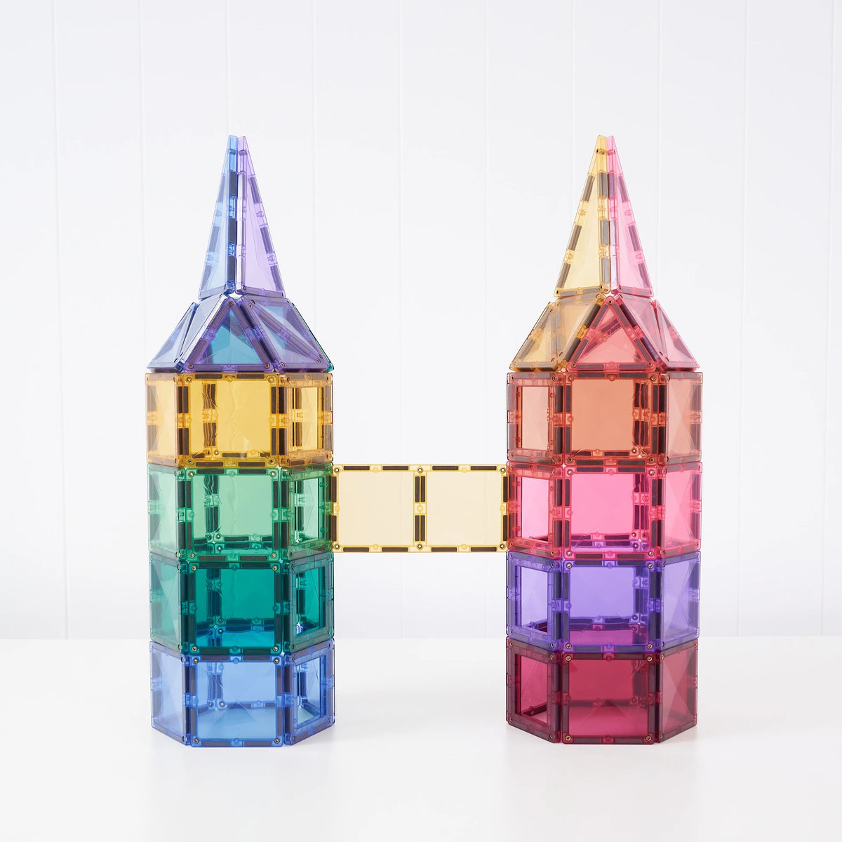 Two colorful magnetic building towers connected by a bridge, made from translucent square tiles in blue, green, purple, yellow, orange, and pink, set against a white background.